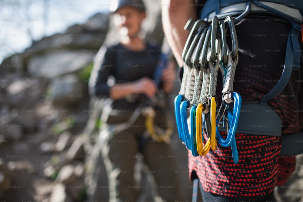 An unrecognizable instructor with harness and carabiners climbing rocks with seniors outdoors in nature, active lifestyle.