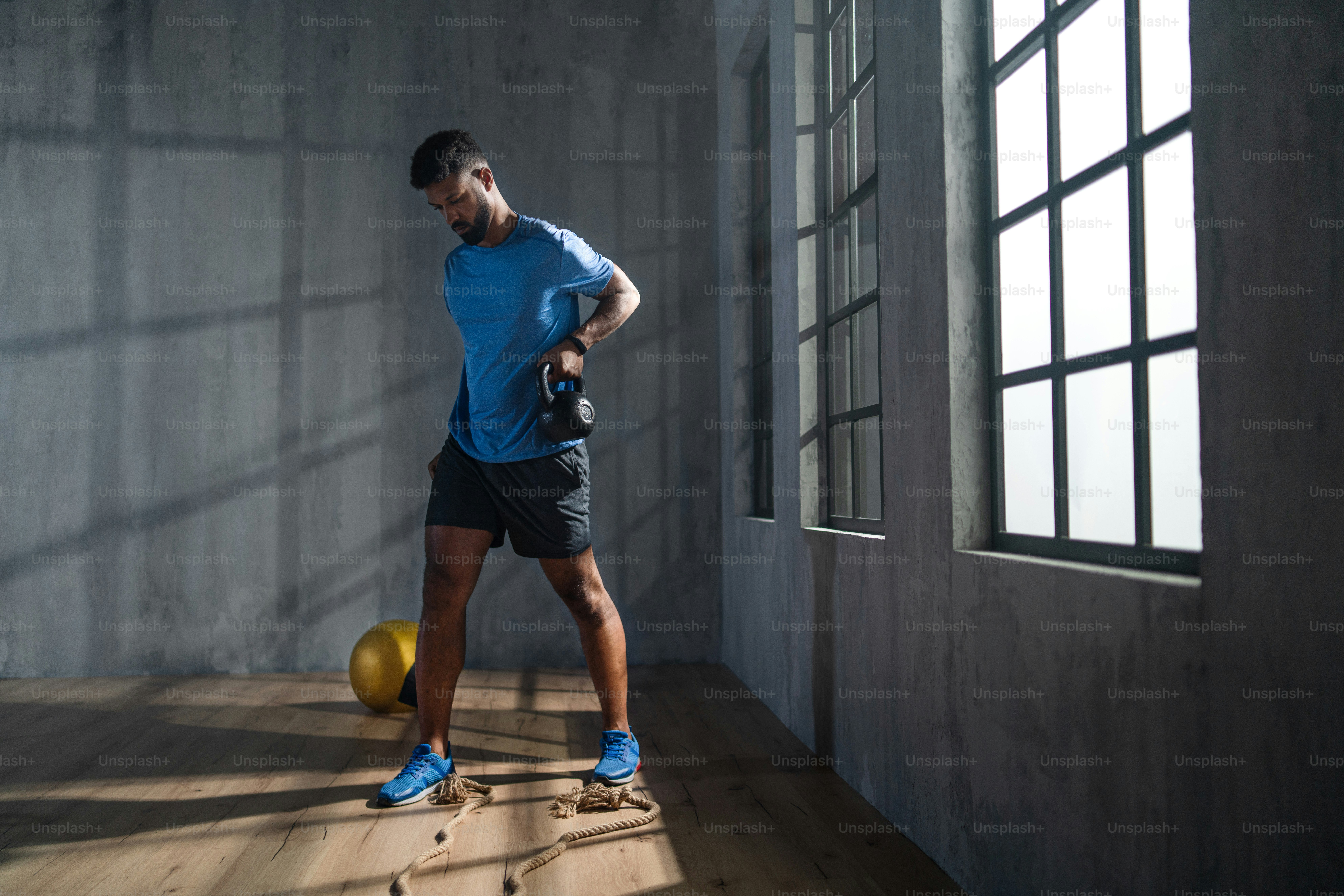 A young African American sportsman standing and lifting a kettle bell indoors, workout training concept.