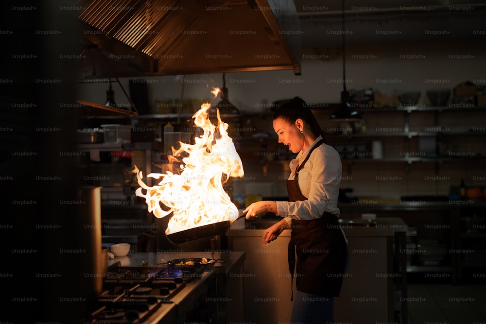 A professional chef preparing meal, flambing indoors in restaurant kitchen.