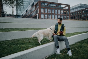 A happy young man lying on grass with his dog outdoors in town.