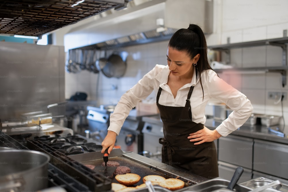A professional female chef preparing meal indoors in restaurant kitchen.