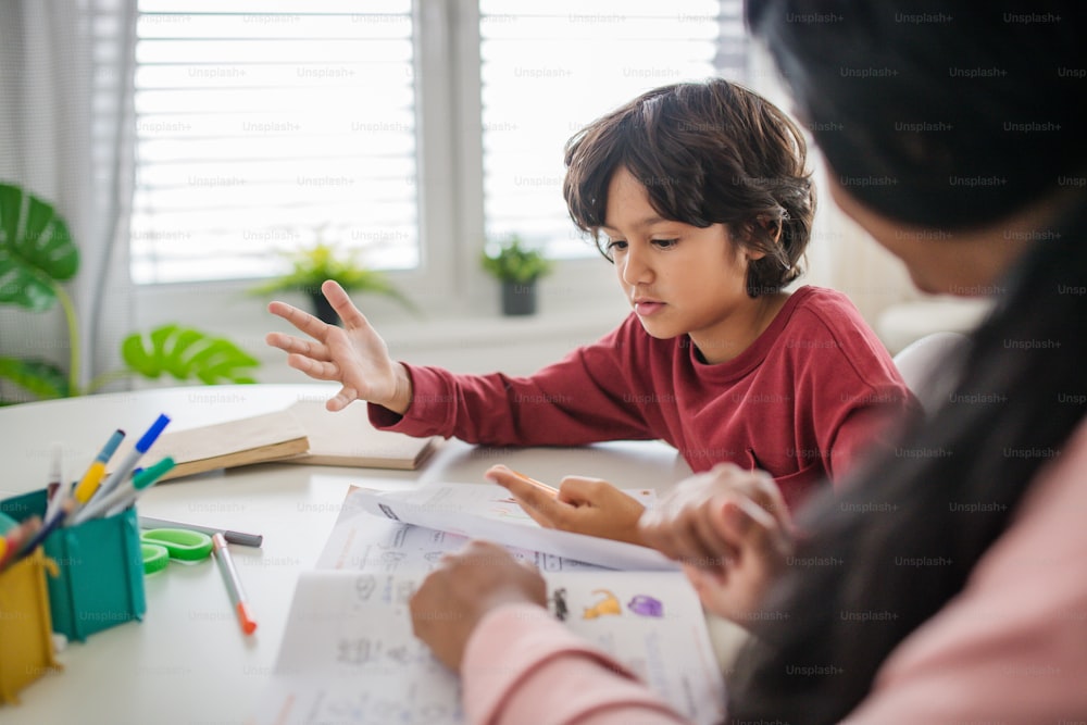 Un petit garçon multiracial faisant ses devoirs avec sa mère à la maison.