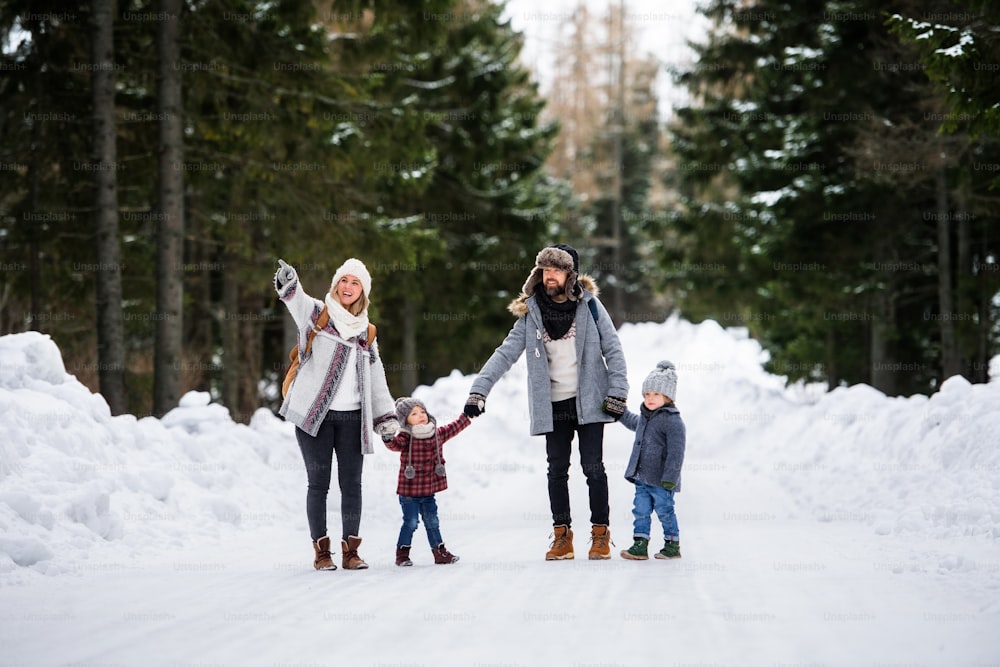 Front view portrait of father and mother with two small children in winter nature, walking in the snow.