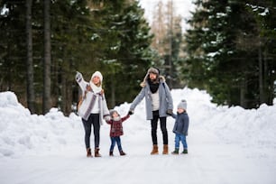 Retrato de vista frontal del padre y la madre con dos niños pequeños en la naturaleza invernal, caminando en la nieve.
