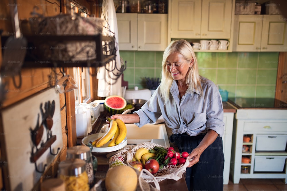 Una donna anziana felice che disfa la spesa al chiuso a casa, stile di vita sostenibile.