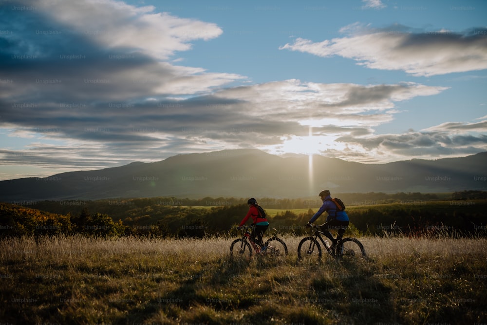 An active senior couple riding bikes outdoors in autumn nature at dusk.