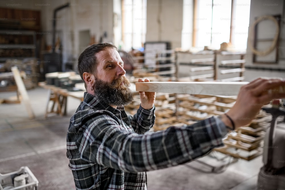 Un carpintero maduro que lleva tablas de madera al interior de un taller de carpintería. Concepto de pequeña empresa.
