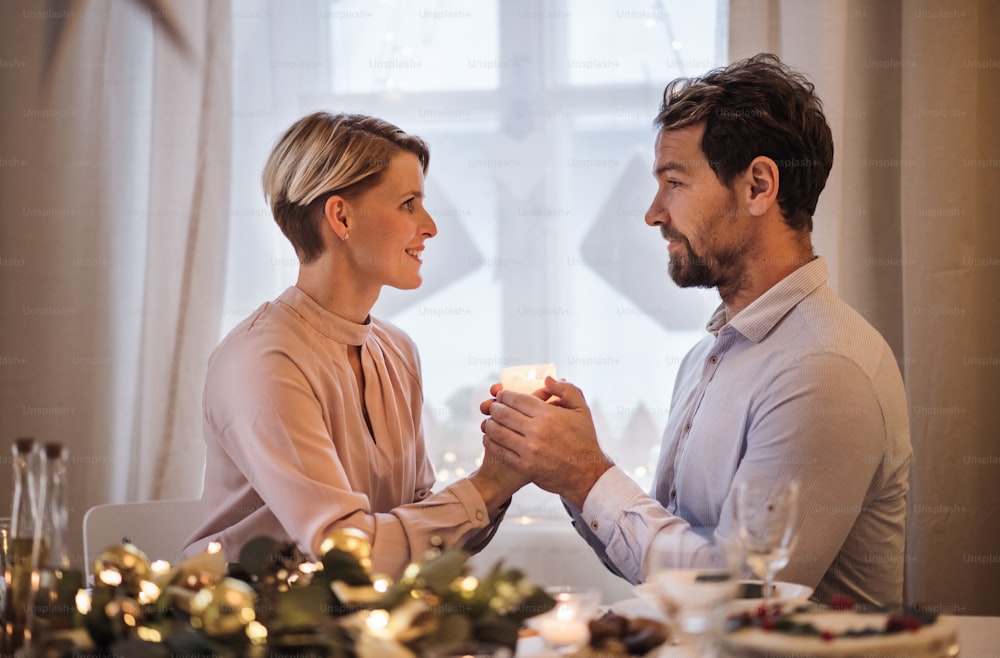 Retrato de vista lateral de una pareja feliz en el interior de la mesa celebrando la Navidad.