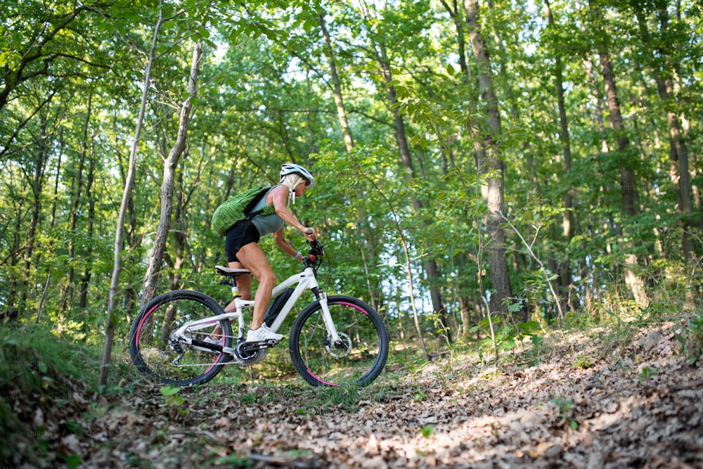 A low angle view of active senior woman biker cycling outdoors in forest.