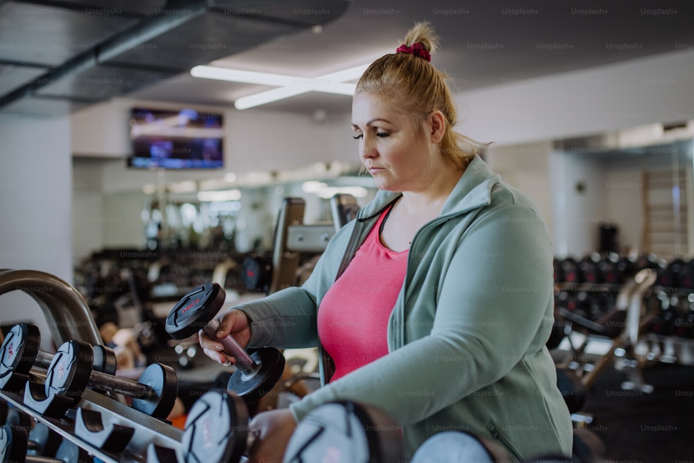 Una mujer de talla grande entrenando tomando mancuernas en el interior del gimnasio