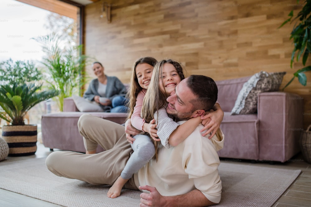 Two happy sisters having fun with a father, lying on his back with mother at background at home