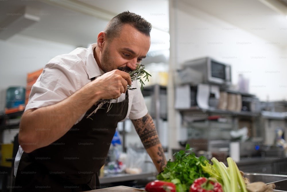 A mature chef smelling herbs in commercial kitchen.