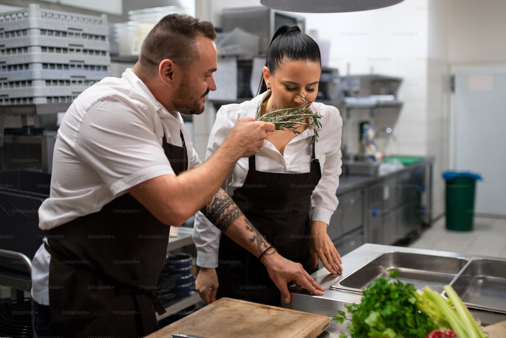 A chef giving herbs to smell to his colleague in commercial kitchen.