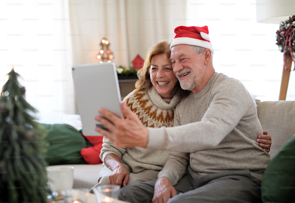 Vista lateral de una feliz pareja de ancianos en el interior de la casa en Navidad, teniendo una videollamada con la familia.