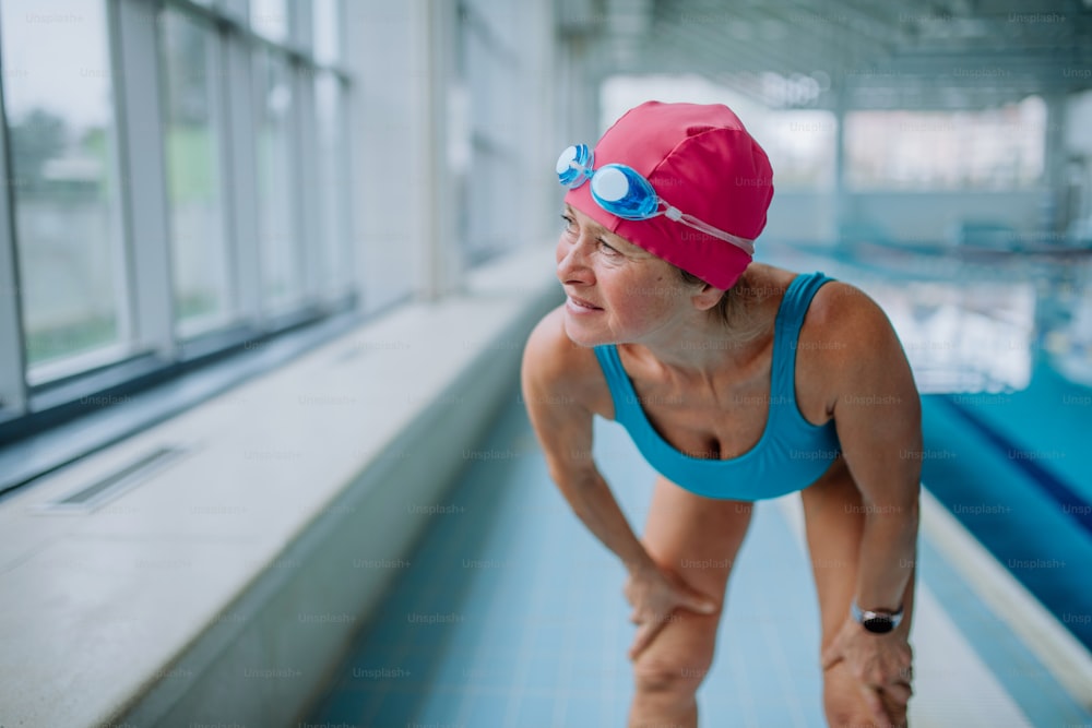An active senior woman preapring for swim in indoors swimming pool.