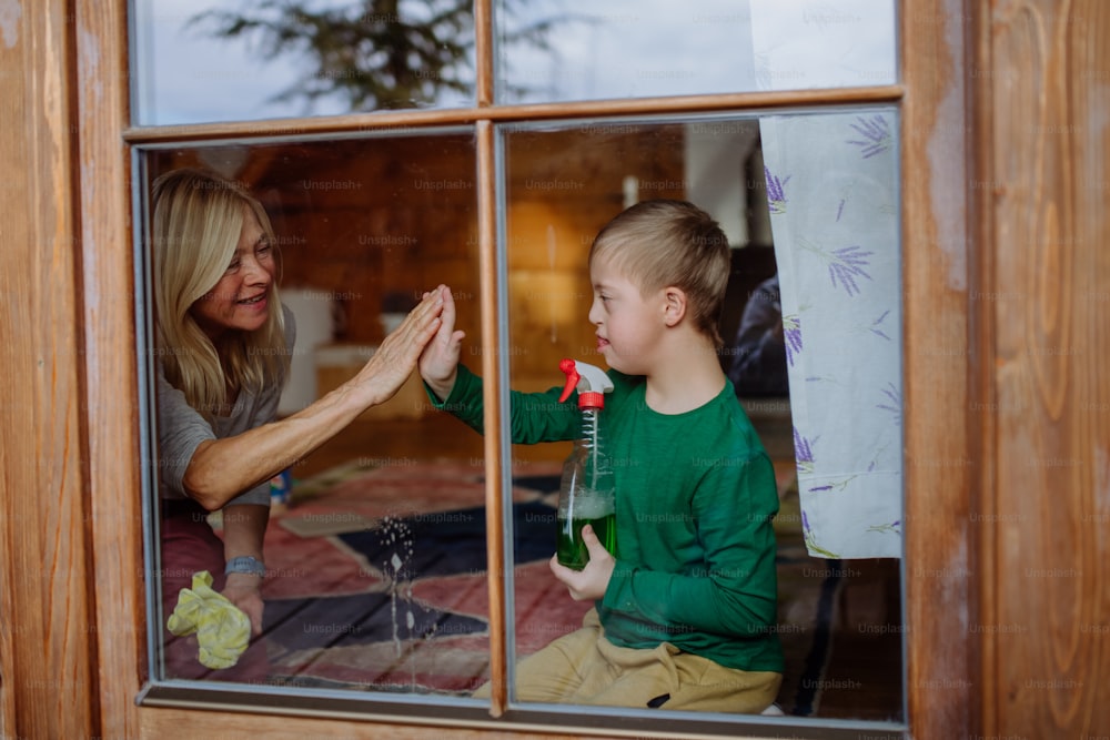 다운 증후군을 앓고있는 소년과 할머니가 집에서 창문을 청소하고 있습니다.