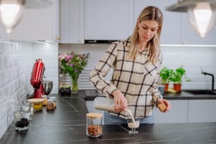 Una donna che versa latte di mandorla in un bicchiere in cucina. Concetto di prodotto vegano sano.