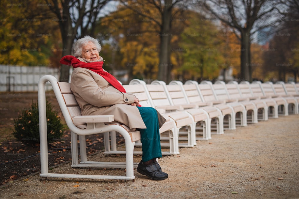 A senior woman sitting on bench in town park in autumn, looking at camera.