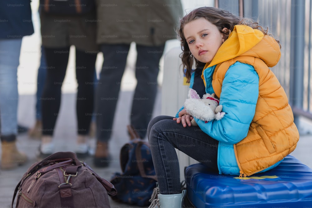 Ein trauriges ukrainisches Einwandererkind mit Gepäck wartet am Bahnhof, ukrainisches Kriegskonzept.