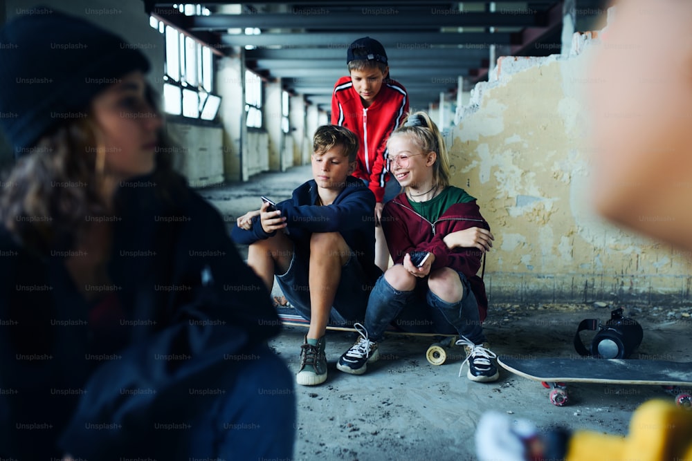 Vista frontal de grupo de adolescentes sentados dentro de casa em prédio abandonado, usando smartphones.