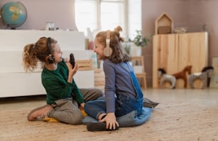 Happy little girls with headphones and microphone taking an interview, having fun and playing at home.