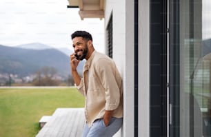 Portrait of young man student with smartphone outdoors on patio at home, making a phone call.