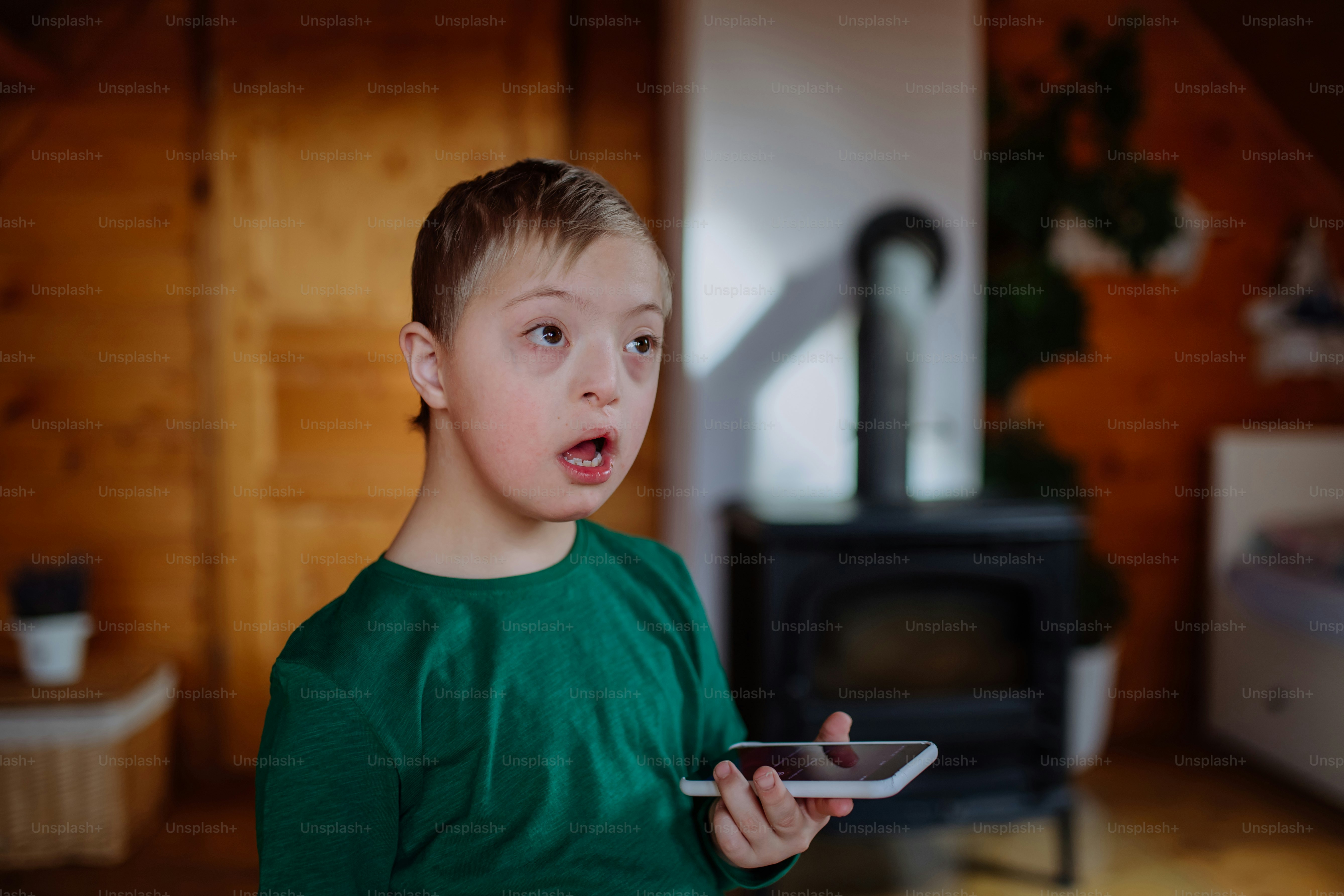 Um garotinho com síndrome de Down sentado no chão e usando smartphone em casa.