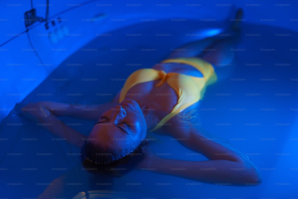 A beautiful woman floating in tank filled with dense salt water used in medical therapy.