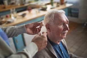 A caregiver helping senior man to insert hearing aid in his ear.