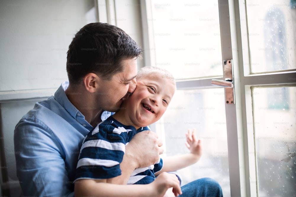 Reifer Vater mit glücklichem Down-Syndrom-Sohn drinnen zu Hause, küsst seine Wange.
