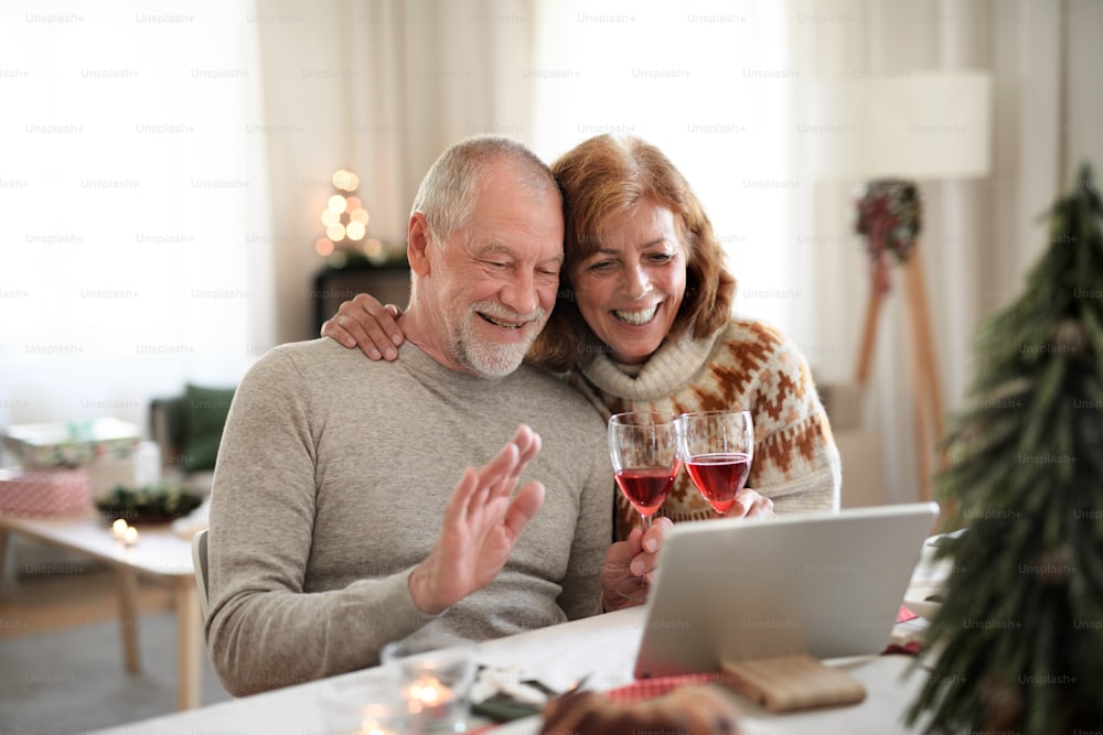 Seniorenpaar mit Wein drinnen zu Hause zu Weihnachten, Videoanruf mit Familie.