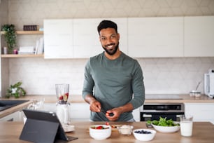 태블릿을 들고 집에서 실내에서 건강한 아침 식사를 준비하는 젊은 남자의 초상화, 홈 오피스 개념.
