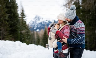 Side view of father and mother with small child in winter nature, standing in the snow.