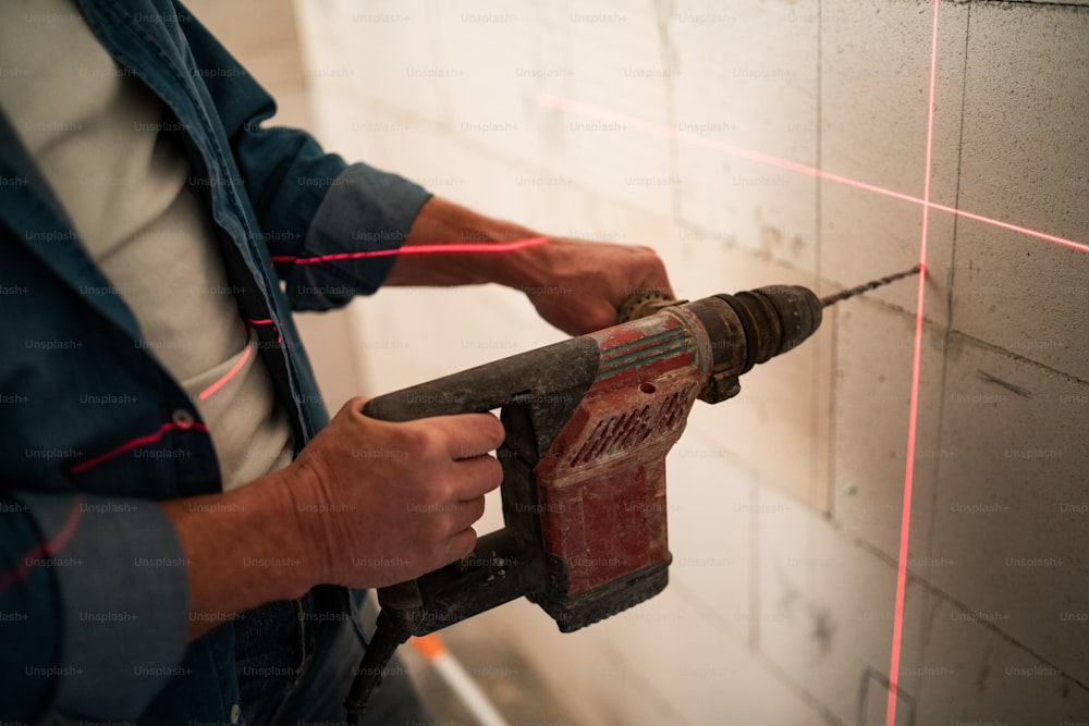 Eine Nahaufnahme des Handwerkers, der mit Hilfe eines Lasernivellierers ein Loch mit Bohrer an der Wand macht