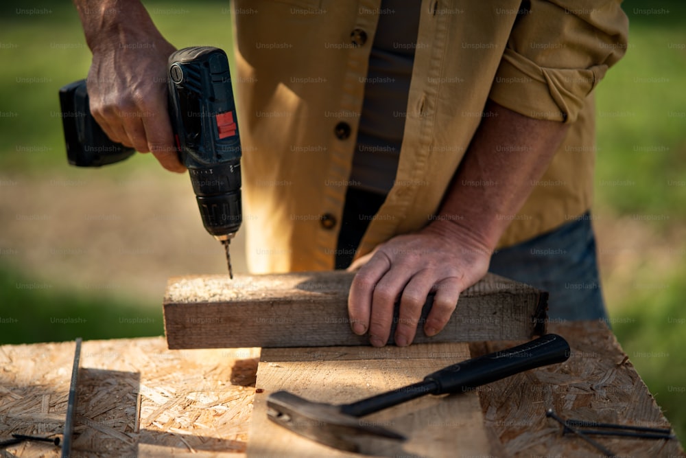 Un gros plan d’un charpentier bricoleur travaillant dans un atelier de bricolage de menuiserie à l’extérieur avec une perceuse.