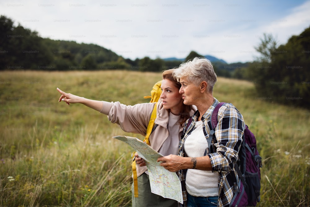 Una mujer adulta media feliz con una madre mayor activa que camina y mira el mapa al aire libre en la naturaleza.