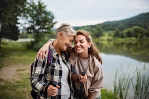 A happy senior mother hiker embracing with adult daughter when looking at lake outdoors in nature