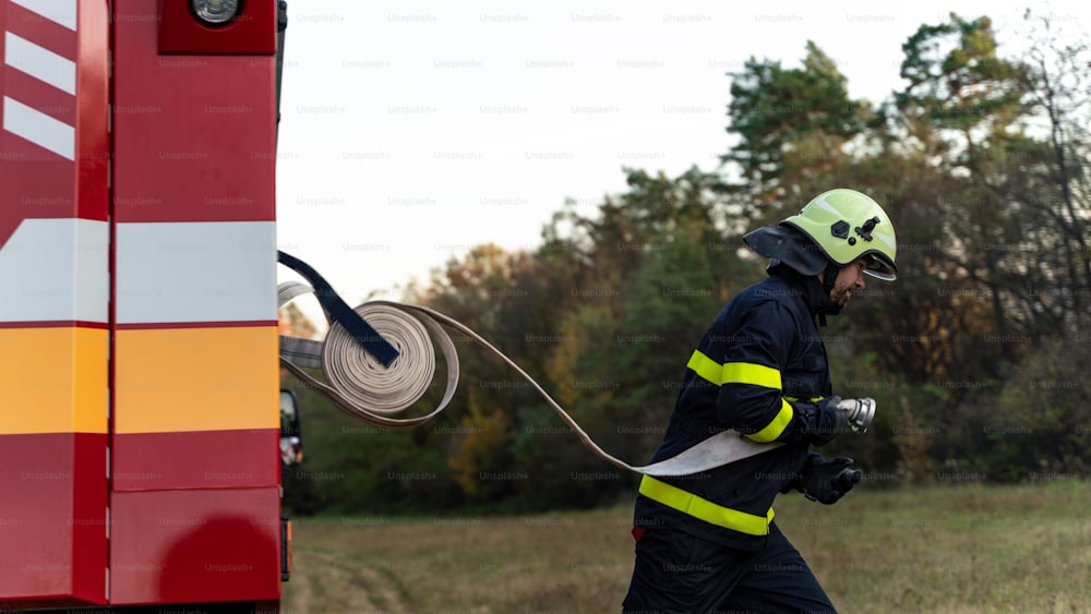 Um bombeiro em ação levando mangueira de caminhão de bombeiros ao ar livre na natureza.