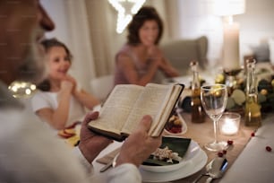 Bambina felice con i nonni seduti in casa che festeggiano insieme il Natale, lettura della Bibbia.