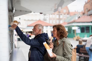 Ein glückliches älteres Paar Touristen kaufen Snack im Freien auf der Straße.