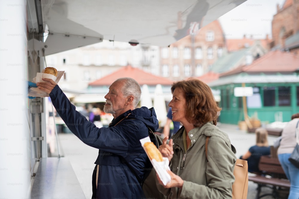 Una coppia di turisti anziani felici che acquistano uno spuntino all'aperto in strada.