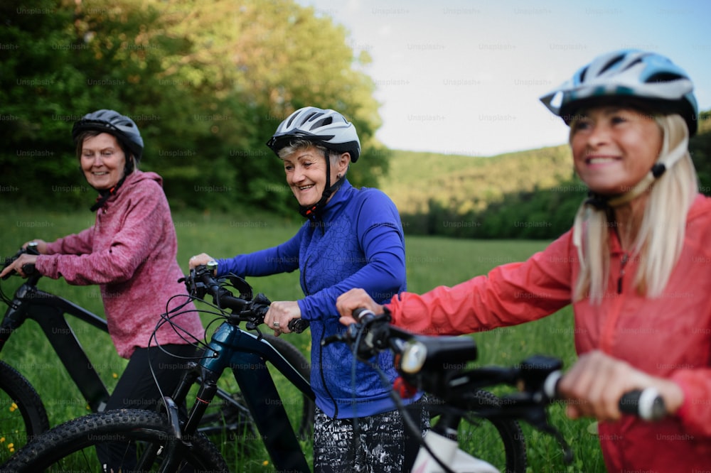 Happy active senior women friends pushing bicycles together outdoors in the nature.