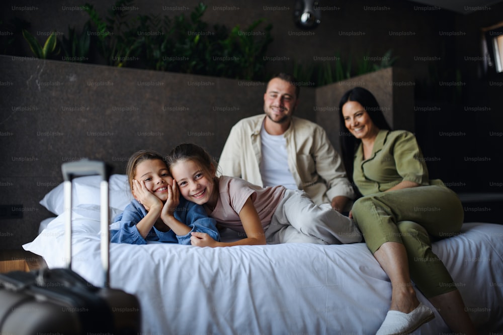 H happy young family with two children lying on bed and looking at camera at hotel, summer holiday.