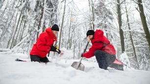 山岳救助隊が冬の屋外で森の中でシャベルで雪を掘る様子をローアングルで撮影。