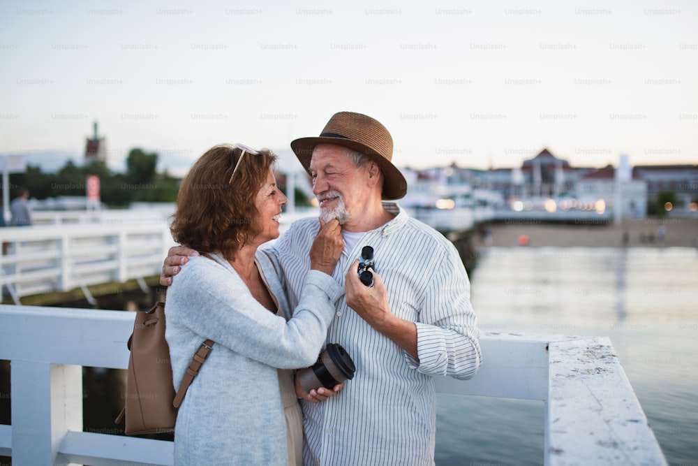 Ein glückliches älteres Paar, das sich draußen am Pier am Meer umarmt und sich gegenseitig ansieht.