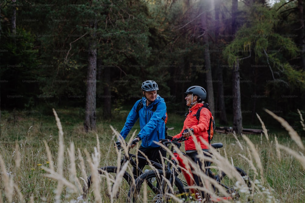 Una feliz pareja de ciclistas mayores abrazando al aire libre en la naturaleza en un día de otoño.