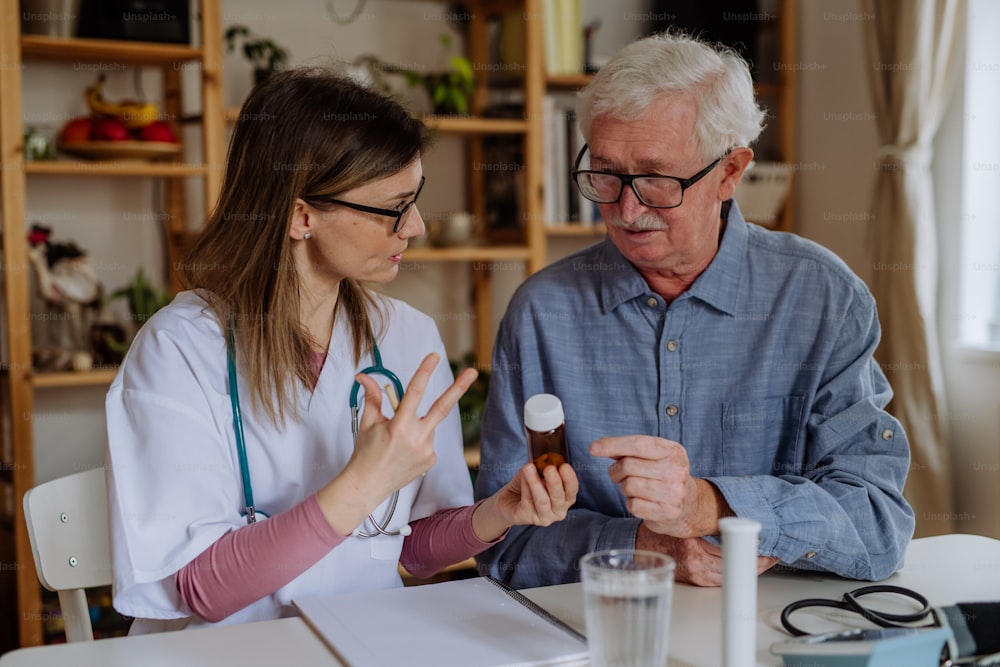 A healthcare worker or caregiver visiting senior man indoors at home, explaining medicine dosage.