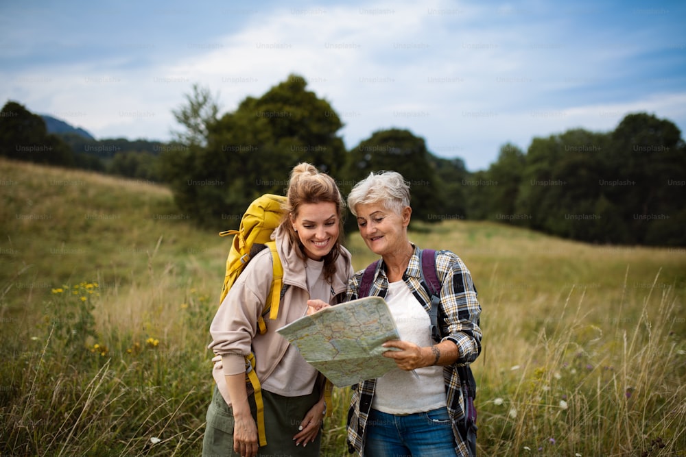 Una mujer adulta media feliz con una madre mayor activa que camina y mira el mapa al aire libre en la naturaleza.