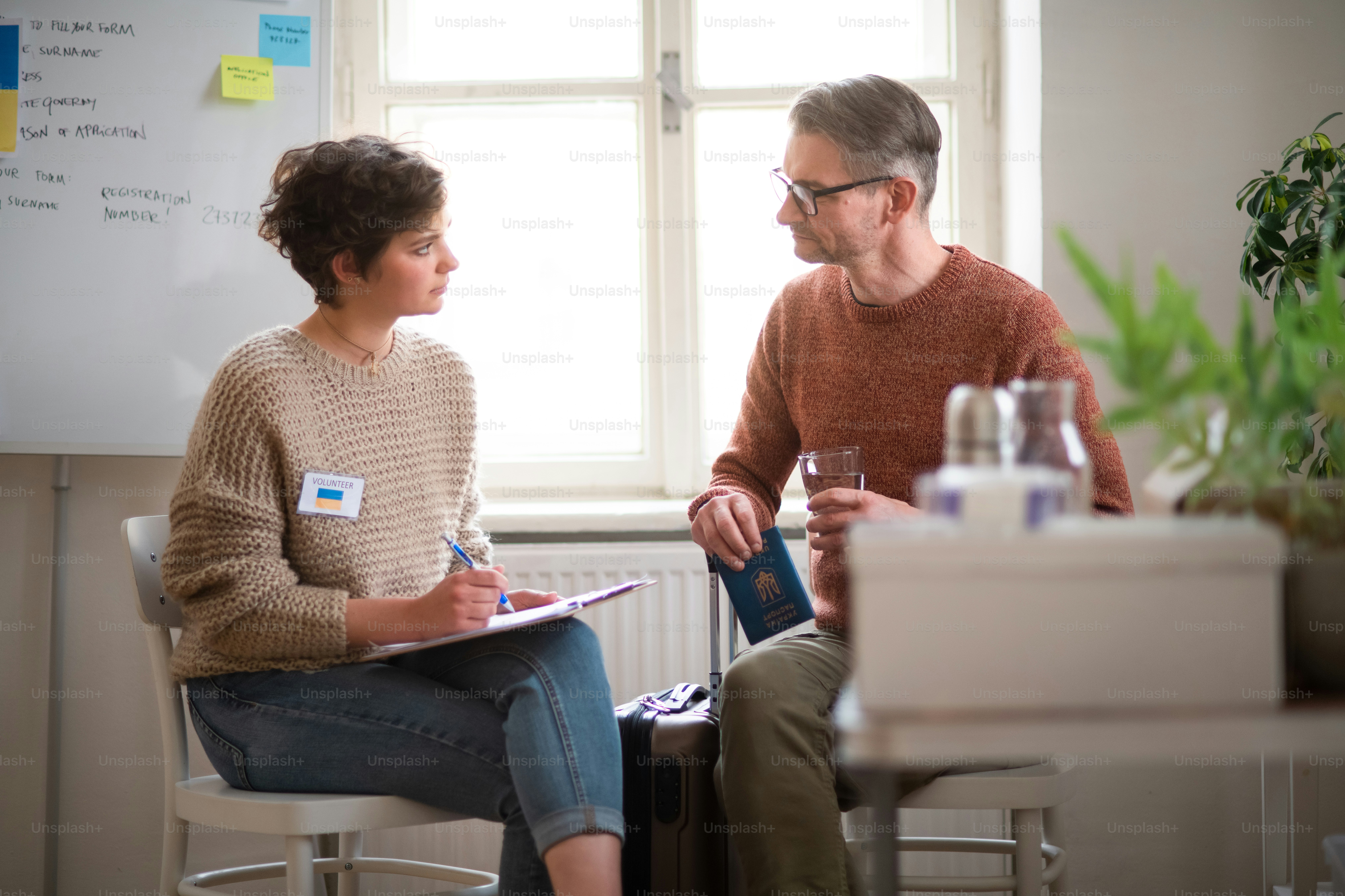 A young woman volunteer helping Ukrainian man to fill in forms at asylum centre.