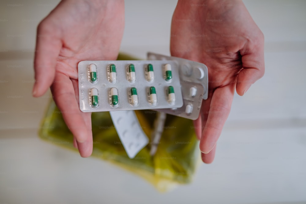 Manos de mujer sosteniendo y tirando ampollas de pastillas caducadas a la basura.